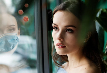 Woman who reflection in the window is wearing a face mask