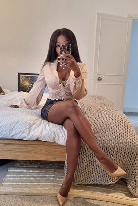 Sexy black girl sitting on a bed taking a selfie