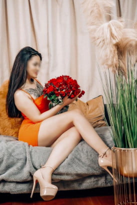 Elegant tattooed brunette in an orange dress holding a big bouquet of red roses